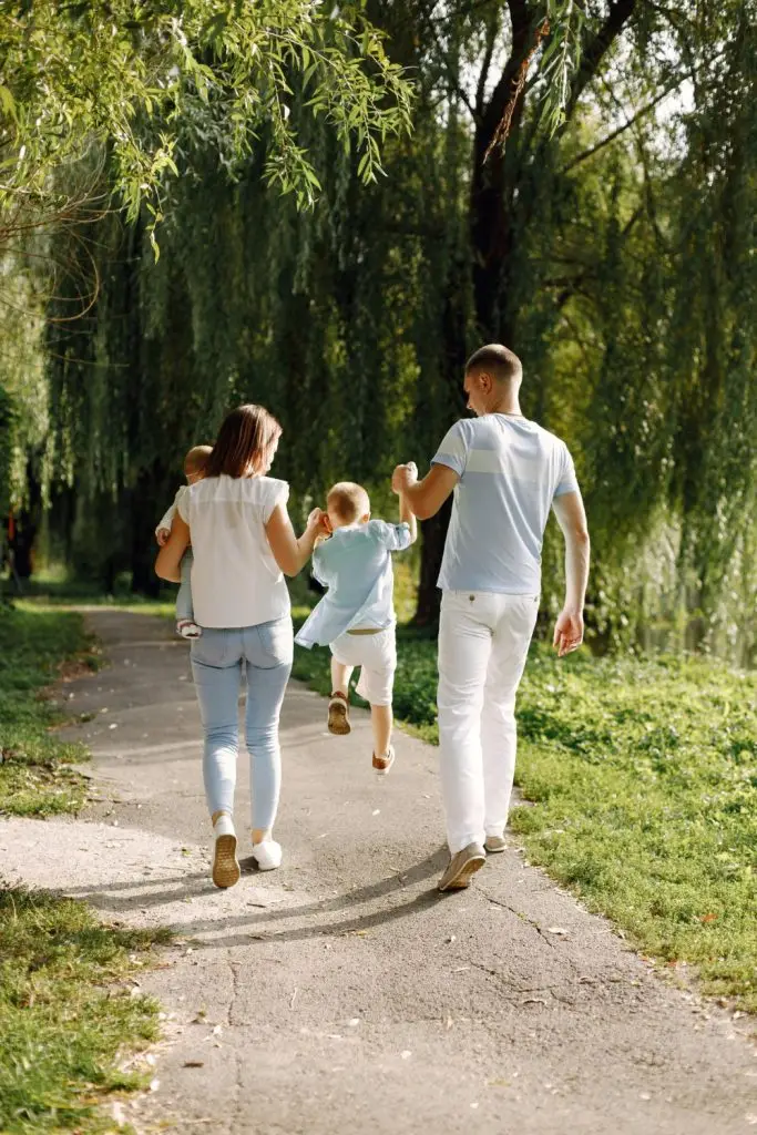 Famille qui marche en s'éloignant. Les parents tiennent leur enfant par la main entre eux et le font sauter.